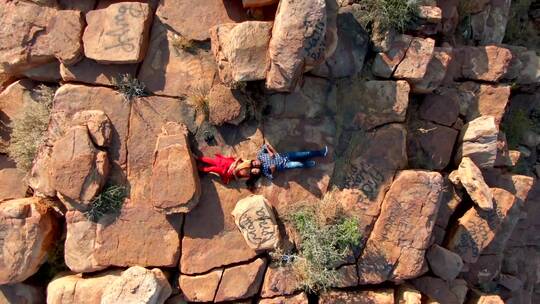航拍一对夫妇躺在岩石山顶