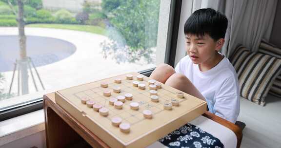 可爱的男孩在窗边下中国象棋