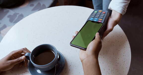 一名妇女正在咖啡馆用智能手机付款，付款处理结账。