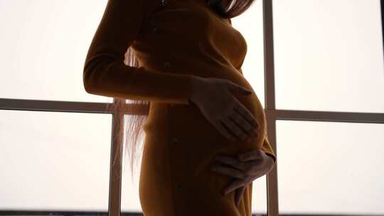 剪影孕妇靠近窗户女性抚摸腹部期待婴儿情绪