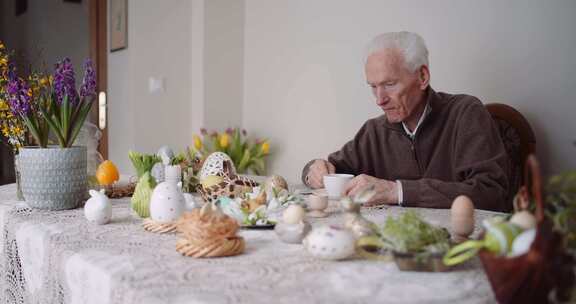 老人坐在复活节彩蛋旁边的一张满桌子旁，用
