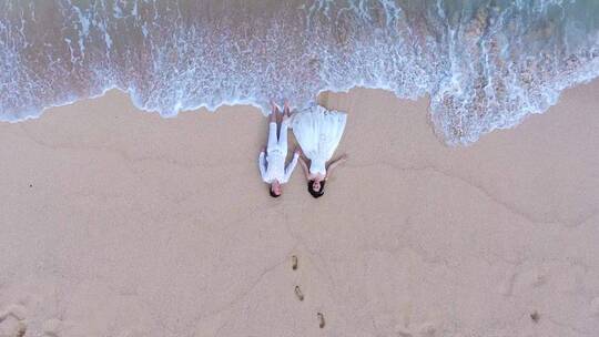 俯拍浪漫情侣躺在沙滩上牵手海浪来袭视频素材模板下载