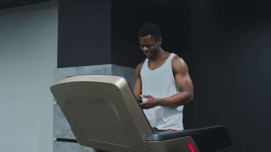 快乐的肌肉发达的非裔美国人在跑步机上行走，在健身房打电话聊天视频素材模板下载