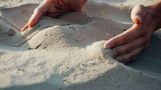 慢动作，关闭：沙子穿过一个年轻女人的手指。沙子正在流淌
