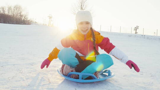 女孩坐雪盘滑下山坡