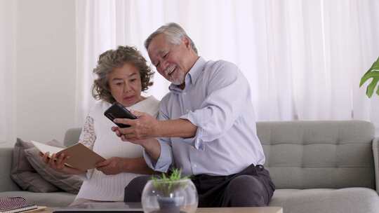 一对亚洲老年人在客厅用智能手机在线视频会议。