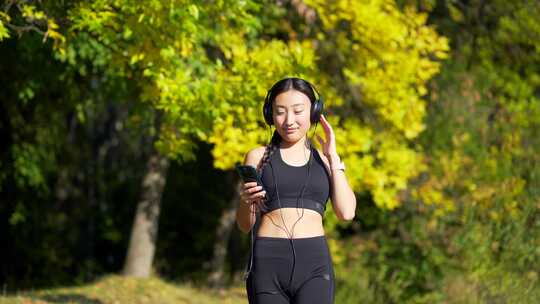 年轻开朗活跃的运动女孩带着耳机走路手机享