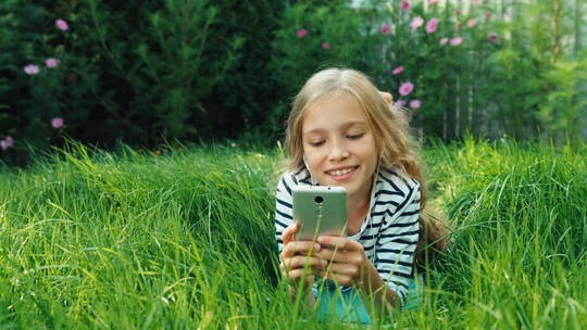 女孩躺在草地上玩智能手机