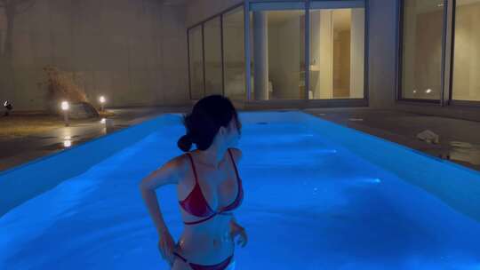 比基尼美女夜晚在度假酒店游泳池中游泳