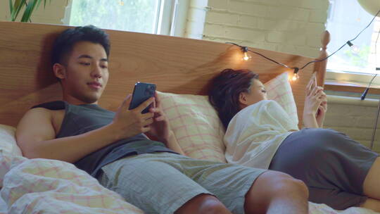 青年情侣坐在床上各自玩手机视频素材模板下载