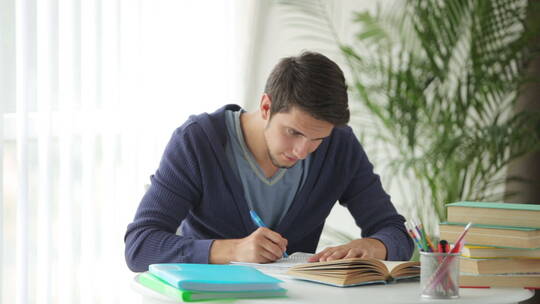 帅哥坐在桌旁学习和写笔记