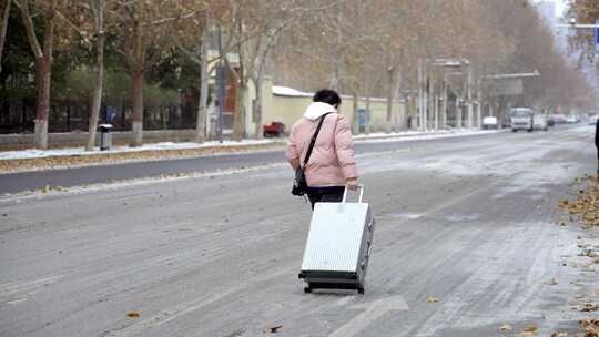 下雪雪地道路泥泞年轻人拉着行李箱赶路背影