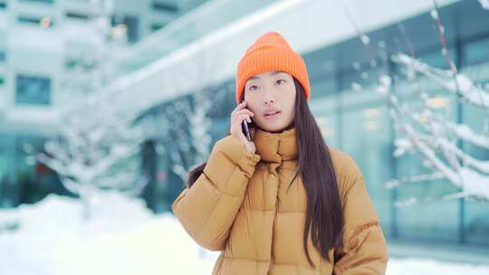 年轻的亚洲女人在手机上说话在一个下雪的冬