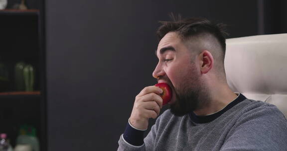 坐在书桌前吃红苹果的男人