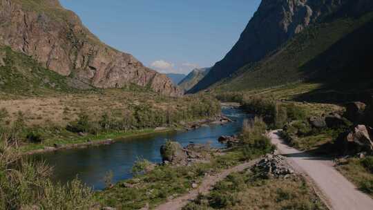 阿尔泰绿色田野和蓝色晴朗天空的山脉之间的Chulyshman河