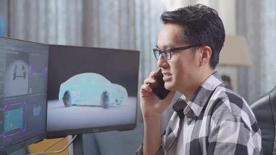 亚洲男设计师在电脑上制作电动汽车3D模型时用智能手机说话