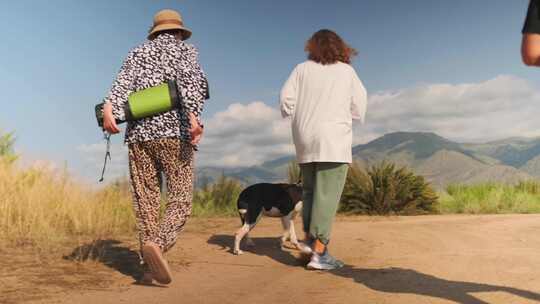 成熟女性牵着斗牛犬在沙漠景观中行走的后视