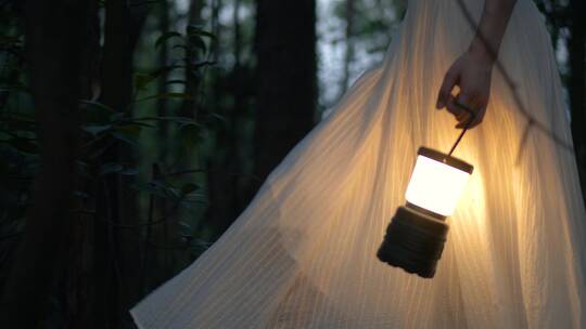 穿白色长裙的女孩提着马灯在黑暗的树林行走视频素材模板下载
