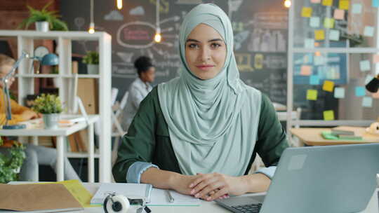 戴头巾的美丽穆斯林妇女坐在办公桌前工作的慢动作肖像