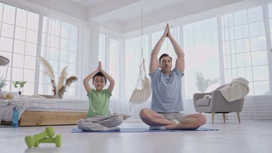 男人和儿子坐在家里的垫子上做瑜伽