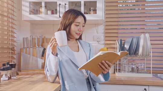 亚洲女人在家里的厨房里喝咖啡，看书。