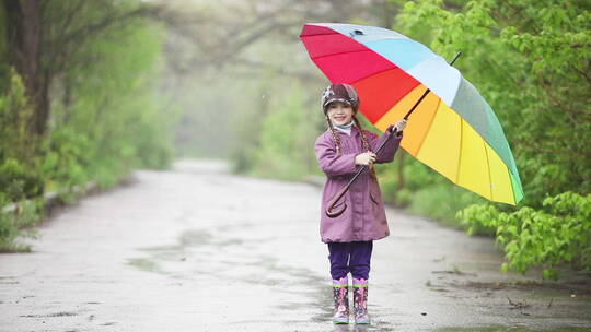 手里拿着雨伞的小女孩在雨中跳跃