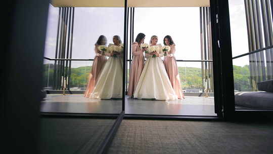 新娘与伴娘在窗前摆姿势微笑的新娘和穿着优