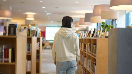 年轻女子图书馆书架前边走边查找书本