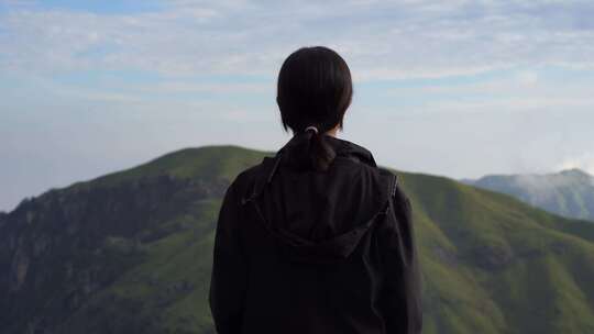 女性青年站在山顶看风景背影看远山感受自然