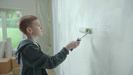 穿着蓝色连帽衫的小男孩正在用油漆滚筒粉刷墙壁视频素材模板下载