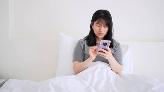 周末早晨年轻都市女孩懒在床上玩手机