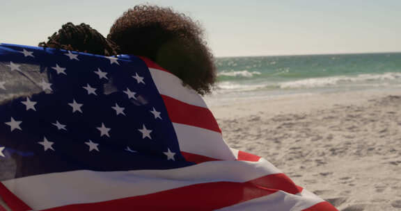 裹着美国国旗的夫妇一起坐在海滩上4k