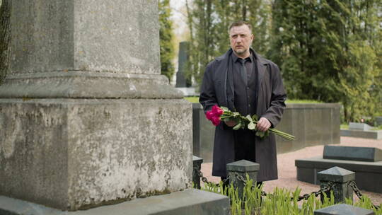 男人拿着鲜花站在墓碑前