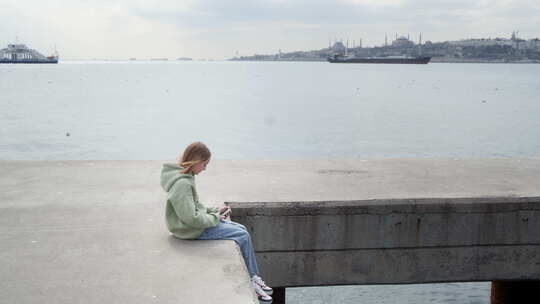 坐在码头上玩手机的孩子
