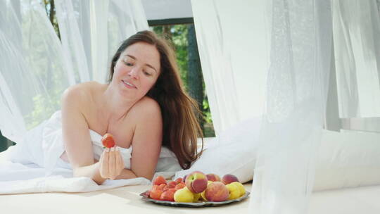 年轻的女人躺在床上拿起水果