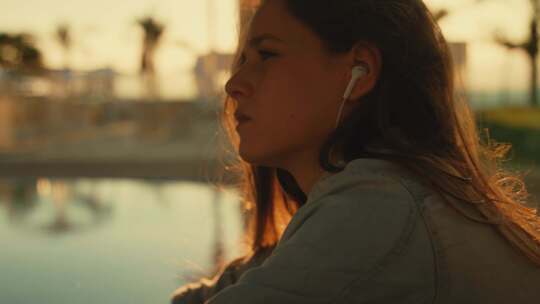 女孩坐在游泳池边通过耳机听音乐