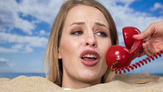 一名女子被埋在沙滩上的沙子里，带着电话
