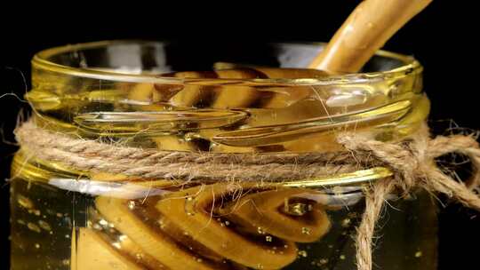 蜂蜜从勺子纺锤上流下来，进入一个黑色背景上有蜂蜜的罐子。