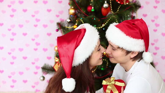 圣诞树旁戴着圣诞帽的情侣