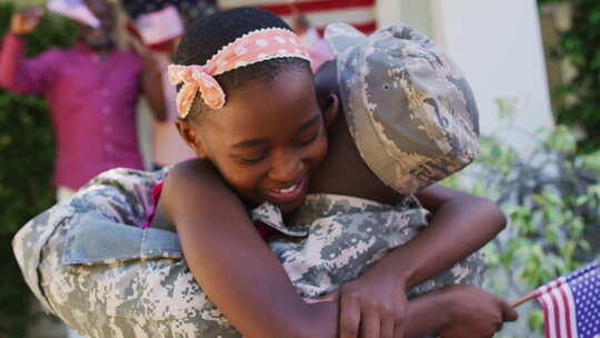 非裔美国士兵父亲拥抱微笑的女儿，背后有家人和美国国旗