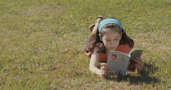 女孩趴在草坪上看书