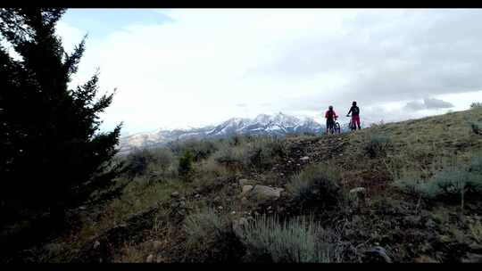 两个骑山地车的女人俯瞰白雪皑皑的山脉和森