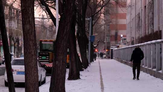 路旁不满积雪的人行道上行走的黑衣男子视频素材模板下载