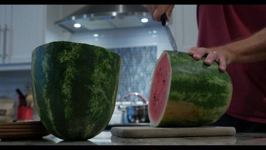 一个人在厨房里用刀切一个大西瓜