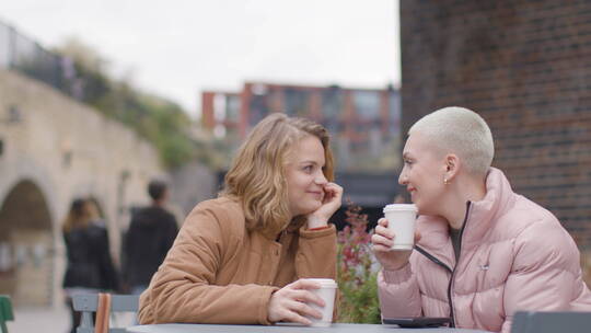 两个女人坐在户外桌子旁喝咖啡聊天
