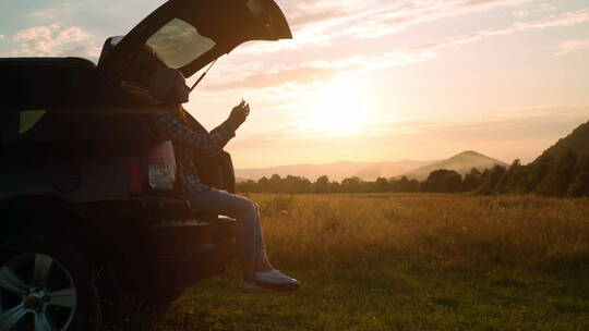 女孩坐在车里拍摄夕阳