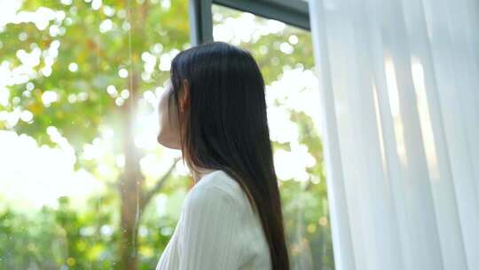 女生早晨起床拉窗帘看窗外