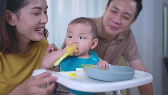 一个小孩吃了他的第一顿饭，父母兴奋地欢呼