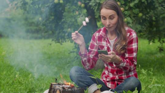 野餐坐在篝火旁吃烧烤的女人