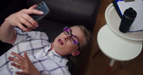 女人躺在沙发上，用手机视频聊天